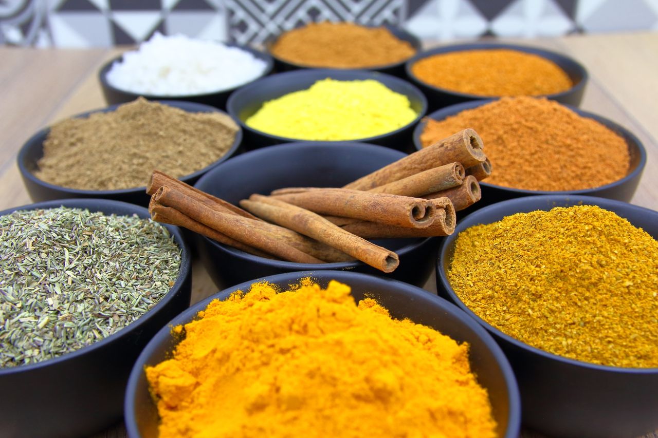 Colorful assortment of spices in bowls with cinnamon sticks on a wooden surface.